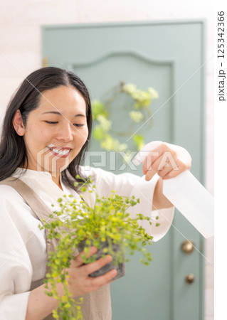 室内で植物の世話をする笑顔の大人女性｜花屋園芸店教室イメージ｜ウェルビー女子｜ウェルビーイング 125342366