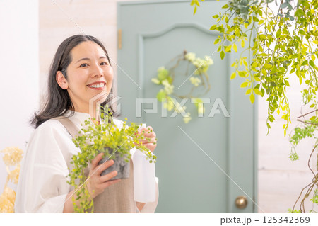 室内で植物の世話をする笑顔の大人女性｜花屋園芸店教室イメージ｜ウェルビー女子｜ウェルビーイング 125342369