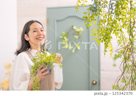 室内で植物の世話をする笑顔の大人女性｜花屋園芸店教室イメージ｜ウェルビー女子｜ウェルビーイング 125342370