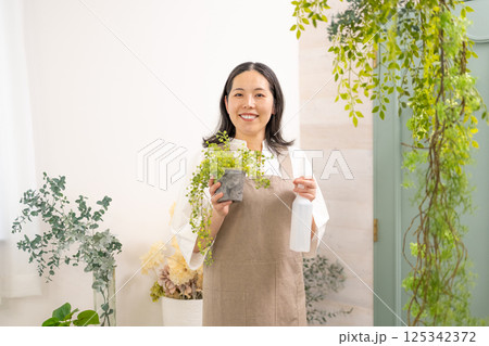 室内で植物の世話をする笑顔の大人女性｜花屋園芸店教室イメージ｜ウェルビー女子｜ウェルビーイング 125342372