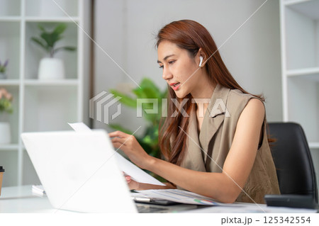Focused Work and Detail Orientation. A woman analyzes documents closely while participating in an online meeting. Focused Work and Detail Orientation. A woman analyzes documents closely while participating in an online meeting. 125342554