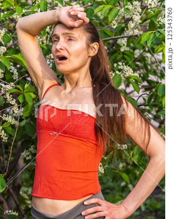 Young woman sneezes in the park against the background of a flowering tree. Allergy to pollen concept. 125343760