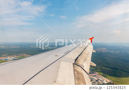 View of airplane wing, blue skies and green land during landing. Airplane window view. 125343825