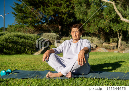 Fit senior woman sitting on yoga mat in park 125344676