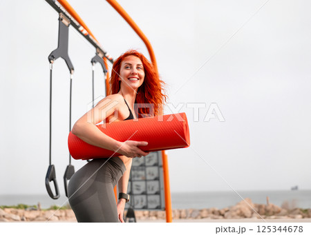 Smiling redhead sportswoman holding yoga mat at 125344678