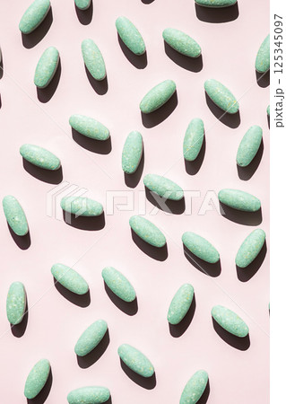 Green Oblong Vitamin Supplement Pills Scattered Across Pink Background with Hard Shadows. Green Oblong Vitamin Supplement Pills Scattered Across Pink Background with Hard Shadows. 125345097
