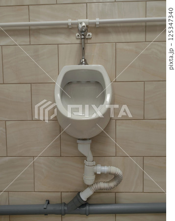 clean white urinal is mounted against beige tiled wall, showcasing contemporary plumbing. clean white urinal is mounted against beige tiled wall, showcasing contemporary plumbing. 125347340
