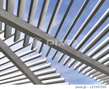 architectural lines wooden pergola contrasted against bright blue sky on sunny day. 125347344
