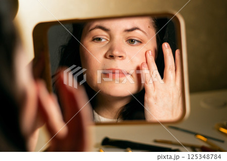 Woman applying face moisturizer cream before make-up and looking in mirror at home. Skin care concept. Self make up. Woman applying face moisturizer cream before make-up and looking in mirror at home. Skin care concept. Self make up. 125348784