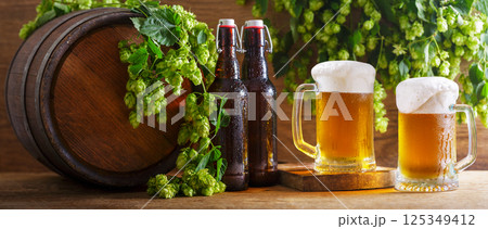 mugs of beer, green hops, bottles and beer barrel on wooden background 125349412