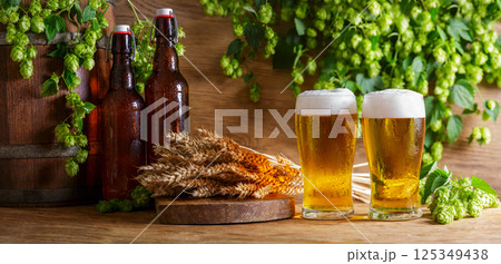 glasses of beer, green hops, bottles, wheat ears and barrel on wooden background 125349438