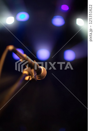 Microphone against blue stage lights. Beams from concert spotlights illuminate the microphone. 125351622