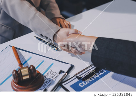 Two businesspeople are shaking hands in a law office with a scale and a gavel on the table Two businesspeople are shaking hands in a law office with a scale and a gavel on the table 125351845