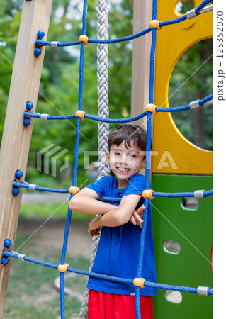 Smiling child posing on climbing net at playground 125352070