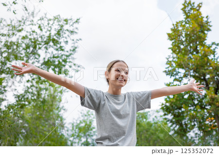 Happy girl embracing nature with open arms in lush green park 125352072