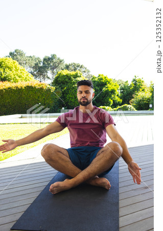 Man meditating on yoga mat outdoors, enjoying peaceful garden surroundings 125352132
