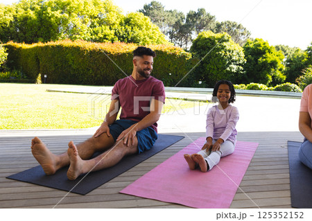 Father and daughter practicing yoga together on mats in sunny backyard 125352152