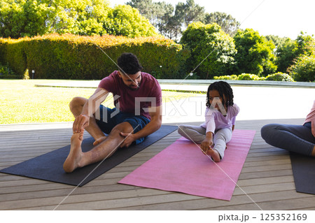 Father and daughter practicing yoga together on mats in sunny backyard 125352169