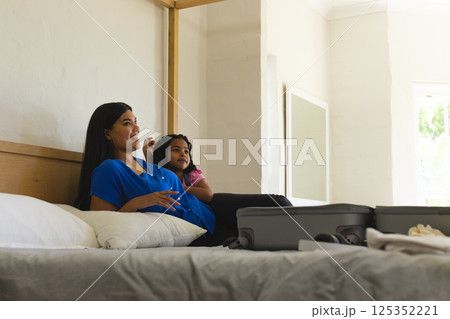 Mother and daughter relaxing on bed with suitcase, enjoying quality time together, copy space Mother and daughter relaxing on bed with suitcase, enjoying quality time together, copy space 125352221