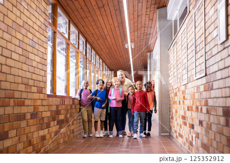Female teacher with diverse group of students standing in school hallway, smiling Female teacher with diverse group of students standing in school hallway, smiling 125352912