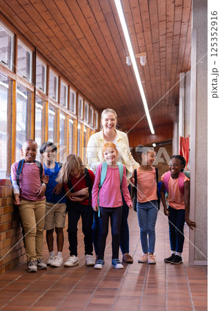Female teacher with diverse group of school children standing in hallway, smiling together Female teacher with diverse group of school children standing in hallway, smiling together 125352916