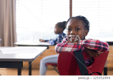 In school, african american girl sitting at desk and smiling, enjoying classroom environment In school, african american girl sitting at desk and smiling, enjoying classroom environment 125352954