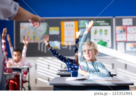 In school, diverse students raising hands in classroom, participating in lesson In school, diverse students raising hands in classroom, participating in lesson 125352991