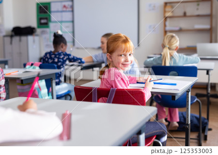 In school, girl smiling and holding pencil while sitting at desk in classroom In school, girl smiling and holding pencil while sitting at desk in classroom 125353003