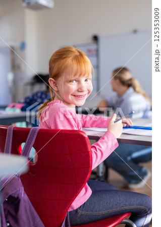 In school, girl smiling and holding pencil while sitting at desk in classroom 125353009