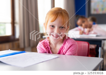 Smiling girl in school classroom sitting at desk with open notebook 125353016