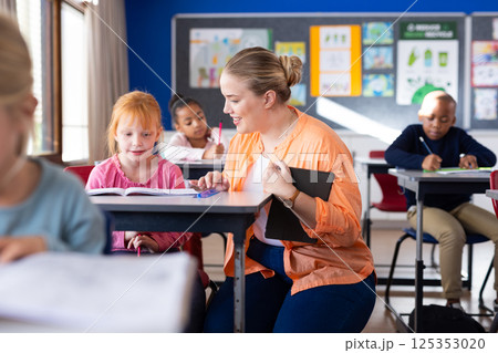 In school, female teacher helping young girl with reading at desk in classroom In school, female teacher helping young girl with reading at desk in classroom 125353020