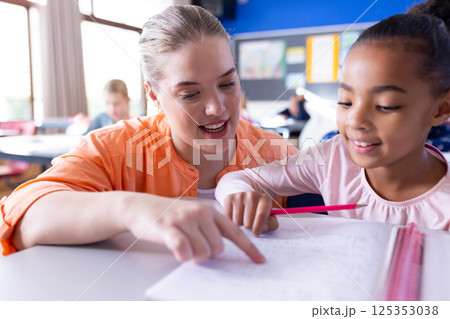 At school, Female teacher helping girl with homework in classroom, focusing on learning together At school, Female teacher helping girl with homework in classroom, focusing on learning together 125353038