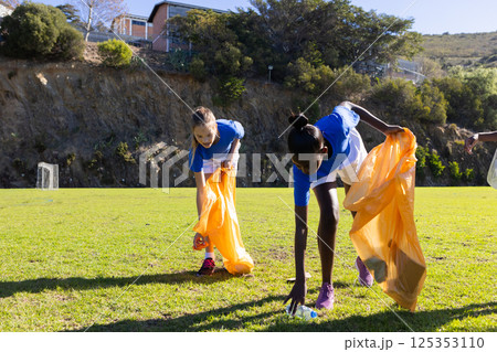 Picking up trash, diverse girls in school uniforms cleaning up field together 125353110