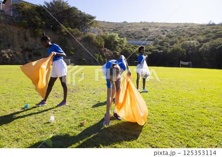 In school, diverse girls picking up trash on field, participating in cleanup activity In school, diverse girls picking up trash on field, participating in cleanup activity 125353114