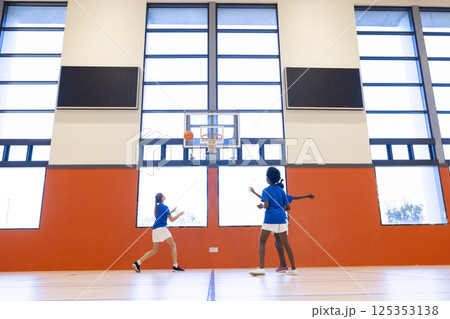 Playing basketball in school gym, diverse girls shooting hoops and practicing teamwork Playing basketball in school gym, diverse girls shooting hoops and practicing teamwork 125353138