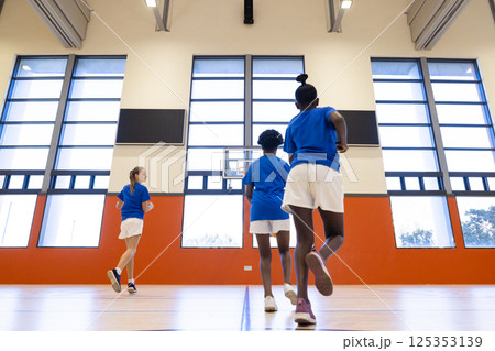 Playing basketball in school gym, diverse girls running towards hoop in uniforms 125353139