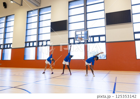 Stretching in gym, three diverse girls in school uniforms exercising together 125353142