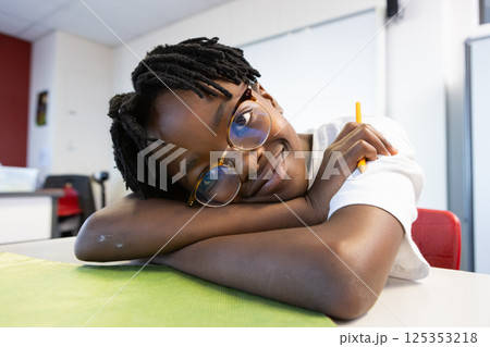 In school, smiling african american boy with glasses holding pencil, resting on desk In school, smiling african american boy with glasses holding pencil, resting on desk 125353218