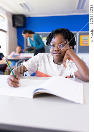 In school, boy writing in notebook while sitting at desk in classroom 125353258