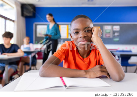 In school, boy sitting at desk with open notebook, smiling at camera 125353260