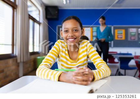Smiling student in classroom with open notebook, Indian female teacher in background 125353261