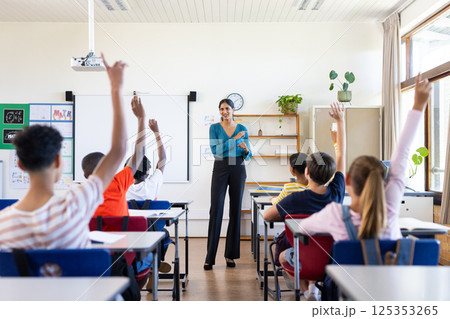 Indian female teacher in classroom, students raising hands to answer question in school 125353265