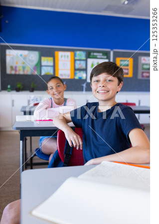 Smiling students sitting at desks in classroom, engaging in school activities 125353266