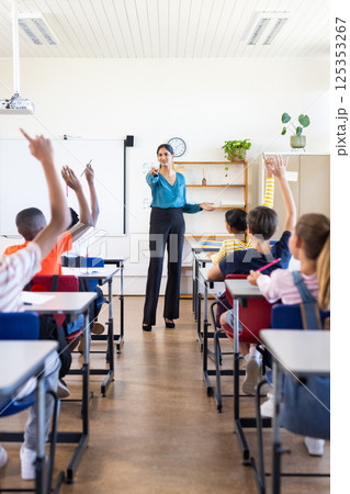 In school, Indian female teacher engaging with students raising hands in classroom 125353267
