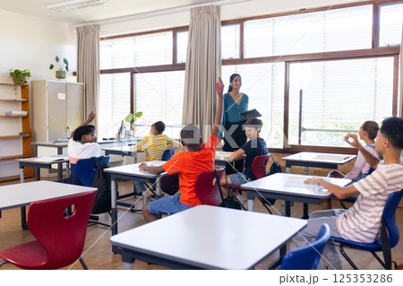 In school, Indian female teacher holding tablet and students raising hands in classroom In school, Indian female teacher holding tablet and students raising hands in classroom 125353286