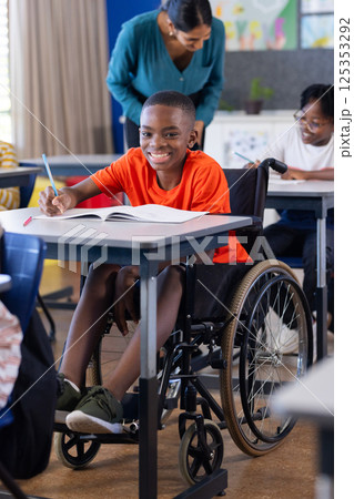 In school, boy in wheelchair writing in notebook, smiling in classroom In school, boy in wheelchair writing in notebook, smiling in classroom 125353292