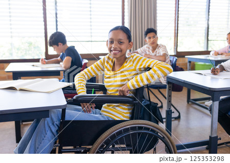 In school, girl in wheelchair smiling and studying with classmates in classroom 125353298