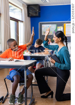 In school, Indian female teacher high-fiving student while holding tablet in classroom 125353307