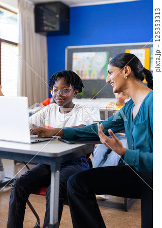 In school, Indian female teacher helping student with laptop in classroom, discussing lesson 125353313