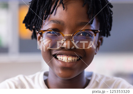 Smiling student wearing glasses in school classroom, looking at camera 125353320